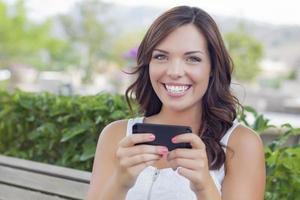 mulher jovem adulta sorridente, mensagens de texto no celular ao ar livre foto