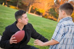 pai hispânico segurando futebol ensinando menino foto