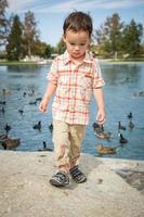 jovem menino chinês e caucasiano se divertindo no parque e lago com patos. foto