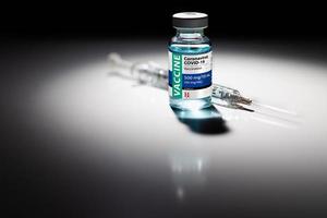 frasco de vacina de coronavírus covid-19 e ponto de seringa iluminado na superfície reflexiva foto