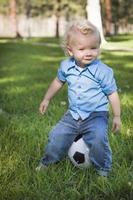 menino bonito brincando com bola de futebol no parque foto