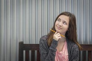 jovem aluna sonhadora com lápis olhando para o lado foto