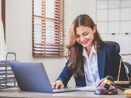 retrato de uma advogada jovem e atraente em um terno preto que lê um caso para o cliente enquanto segura uma caneta e um laptop e trabalha com um martelo no escritório. conceito de advogado. foto