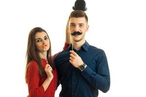 casal jovem encantador confrontado com detalhes de papel como lábios, bigode e chapéus para uma foto