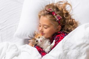 uma menina bonitinha está dormindo docemente em casa em um coelho com um gatinho. roupa de cama de algodão branco. Férias de natal. crianças e animais de estimação em casa. foto de alta qualidade