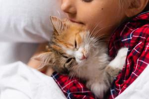 uma menina bonitinha está dormindo docemente em casa em um coelho com um gatinho. roupa de cama de algodão branco. Férias de natal. crianças e animais de estimação em casa. foto de alta qualidade