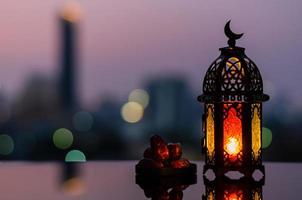 lanterna que tem o símbolo da lua no topo e pequeno prato de frutas tâmaras com céu crepuscular e fundo de luz bokeh da cidade para a festa muçulmana do mês sagrado do ramadã kareem. foto