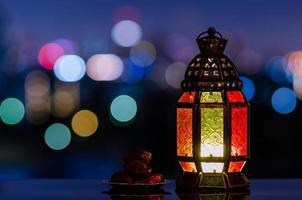 lanterna e pequeno prato de frutas tâmaras com céu noturno e cidade bokeh luz de fundo para a festa muçulmana do mês sagrado do ramadã kareem. foto