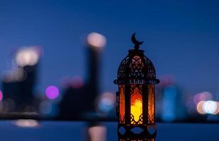 foco seletivo da lanterna que tem o símbolo da lua no topo com o fundo da cidade para a festa muçulmana do mês sagrado do ramadã kareem. foto