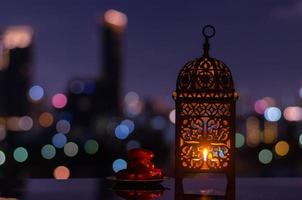 lanterna e pequeno prato de frutas tâmaras com céu noturno e cidade bokeh luz de fundo para a festa muçulmana do mês sagrado do ramadã kareem. foto