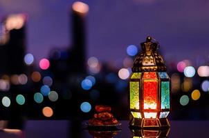 lanterna e pequeno prato de frutas tâmaras com céu noturno e cidade bokeh luz de fundo para a festa muçulmana do mês sagrado do ramadã kareem. foto