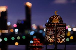 lanterna e pequeno prato de frutas tâmaras com céu noturno e cidade bokeh luz de fundo para a festa muçulmana do mês sagrado do ramadã kareem.