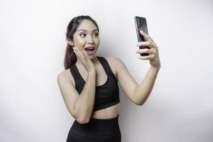 um retrato de uma mulher asiática desportiva vestindo um sportswear e segurando seu telefone, isolado por fundo branco foto