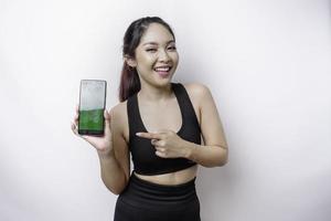 um retrato de uma mulher asiática desportiva vestindo um sportswear e mostrando tela verde em seu telefone, isolado por fundo branco foto