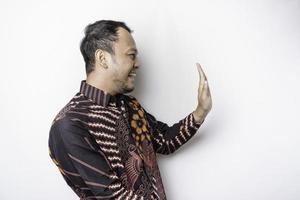 homem asiático animado vestindo camisa batik apontando para o espaço da cópia ao lado dele, isolado pelo fundo branco foto
