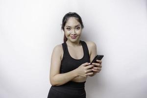 um retrato de uma mulher asiática desportiva vestindo um sportswear e segurando seu telefone, isolado por fundo branco foto