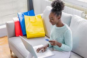 linda mulher negra comprando online com cartão de crédito. mulher segurando o cartão de crédito e usando o laptop. conceito de compras online foto