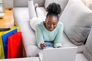 linda mulher negra comprando online com cartão de crédito. mulher segurando o cartão de crédito e usando o laptop. conceito de compras online foto