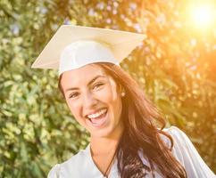 feliz graduando-se menina de raça mista em boné e vestido foto