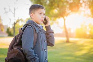 jovem rapaz hispânico caminhando ao ar livre com mochila falando no celular foto