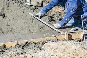 trabalhador de construção de piscina trabalhando com uma haste mais lisa em concreto molhado foto