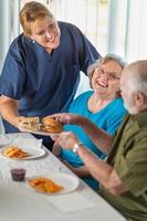 médica ou enfermeira servindo sanduíches de casal adulto sênior na mesa foto