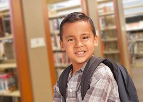 menino estudante hispânico com mochila na biblioteca foto