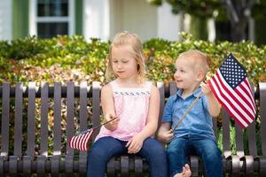 jovem irmã e irmão comparando o tamanho da bandeira americana no banco do parque foto