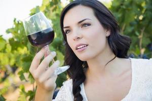 jovem adulta desfrutando de uma taça de vinho no vinhedo foto