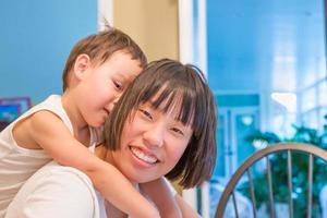 menino chinês e caucasiano de raça mista feliz se divertindo com a mãe chinesa dentro de casa foto