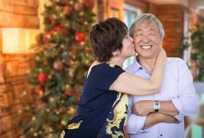 casal chinês sênior feliz beijando na frente da árvore de natal decorada. foto