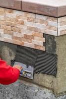 trabalhador instalando cimento de azulejo de parede com espátula e azulejo no canteiro de obras foto