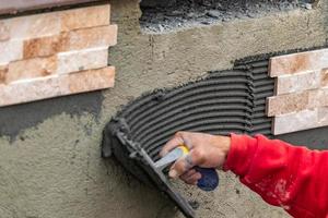 trabalhador instalando cimento de azulejo de parede com espátula e azulejo no canteiro de obras foto