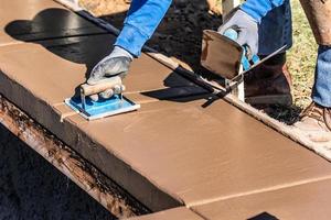 trabalhador da construção civil usando sulcador de mão em cimento úmido formando coping em torno de uma nova piscina foto