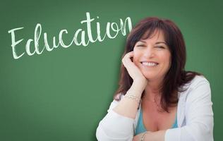 educação escrita na lousa verde atrás de uma mulher sorridente de meia idade foto
