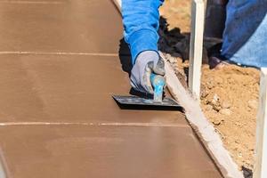 trabalhador da construção civil usando sulcador de mão em cimento úmido formando coping em torno de uma nova piscina foto