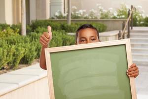 menino com polegares para cima segurando quadro de giz em branco no campus foto