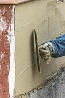 trabalhador de azulejo aplicando cimento com espátula no canteiro de obras da piscina foto