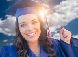 feliz graduando-se mulher de raça mista em boné e vestido foto