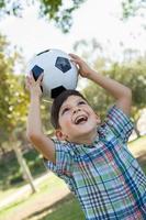 menino bonitinho brincando com bola de futebol ao ar livre no parque. foto