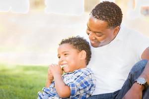 pai afro-americano e filho mestiço comendo uma maçã no parque foto