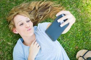 jovem adulta deitada na grama tirando uma selfie com seu telefone inteligente. foto