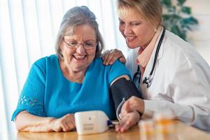 mulher adulta sênior aprendendo com a médica a usar a máquina de pressão arterial foto