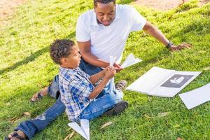 feliz pai afro-americano e filho mestiço brincando com aviões de papel no parque foto