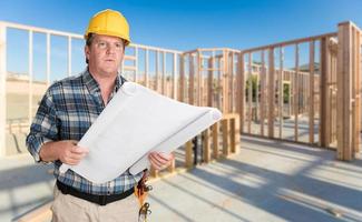 empreiteiro masculino com planos de casa usando capacete dentro do enquadramento de construção de casa nova foto