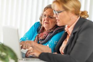 mulher ajudando senhora adulta sênior no computador portátil foto