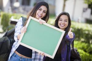 estudantes do sexo feminino de raça mista com polegares para cima segurando lousa em branco foto