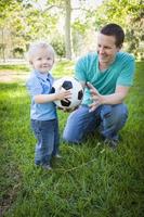 menino e pai brincando com bola de futebol no parque foto