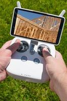 mãos segurando o controlador de quadcopter drone com estrutura de casa de construção na tela foto