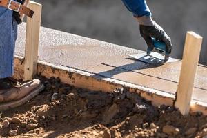 trabalhador da construção civil usando biselador de aço inoxidável em cimento úmido formando cobertura ao redor da nova piscina foto